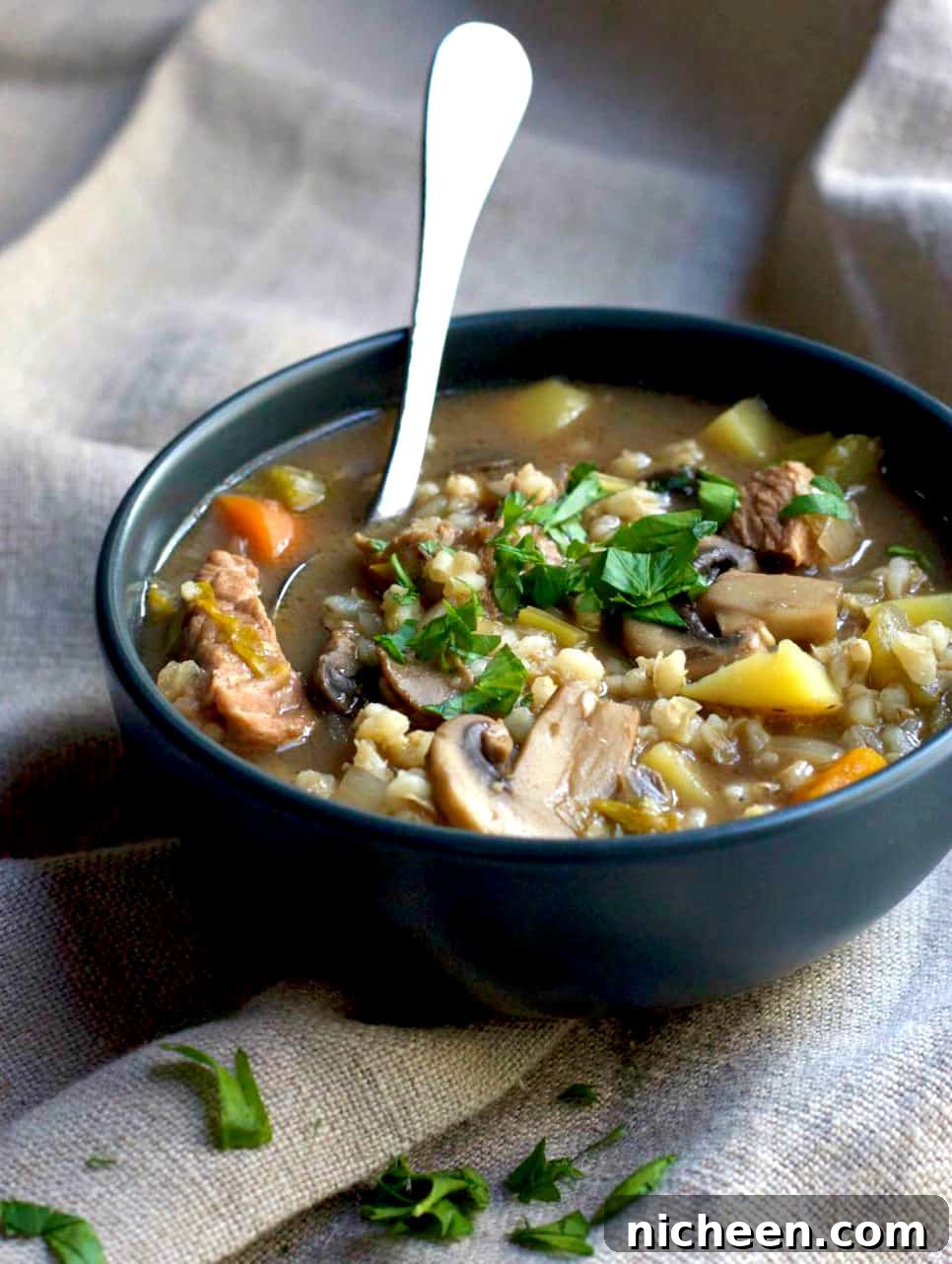 Slow Cooker Beef and Barley Soup in a bowl with a spoon sticking out. 