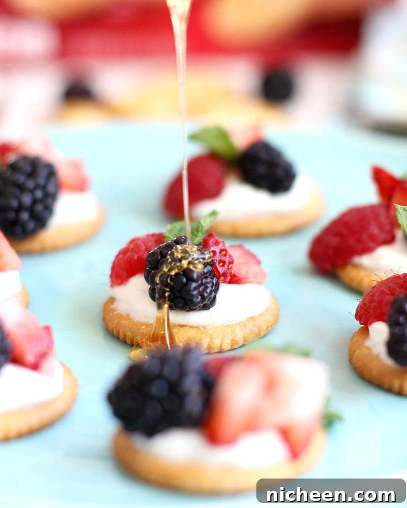 Ritz Crackers being topped with berries and cream and drizzled with honey.