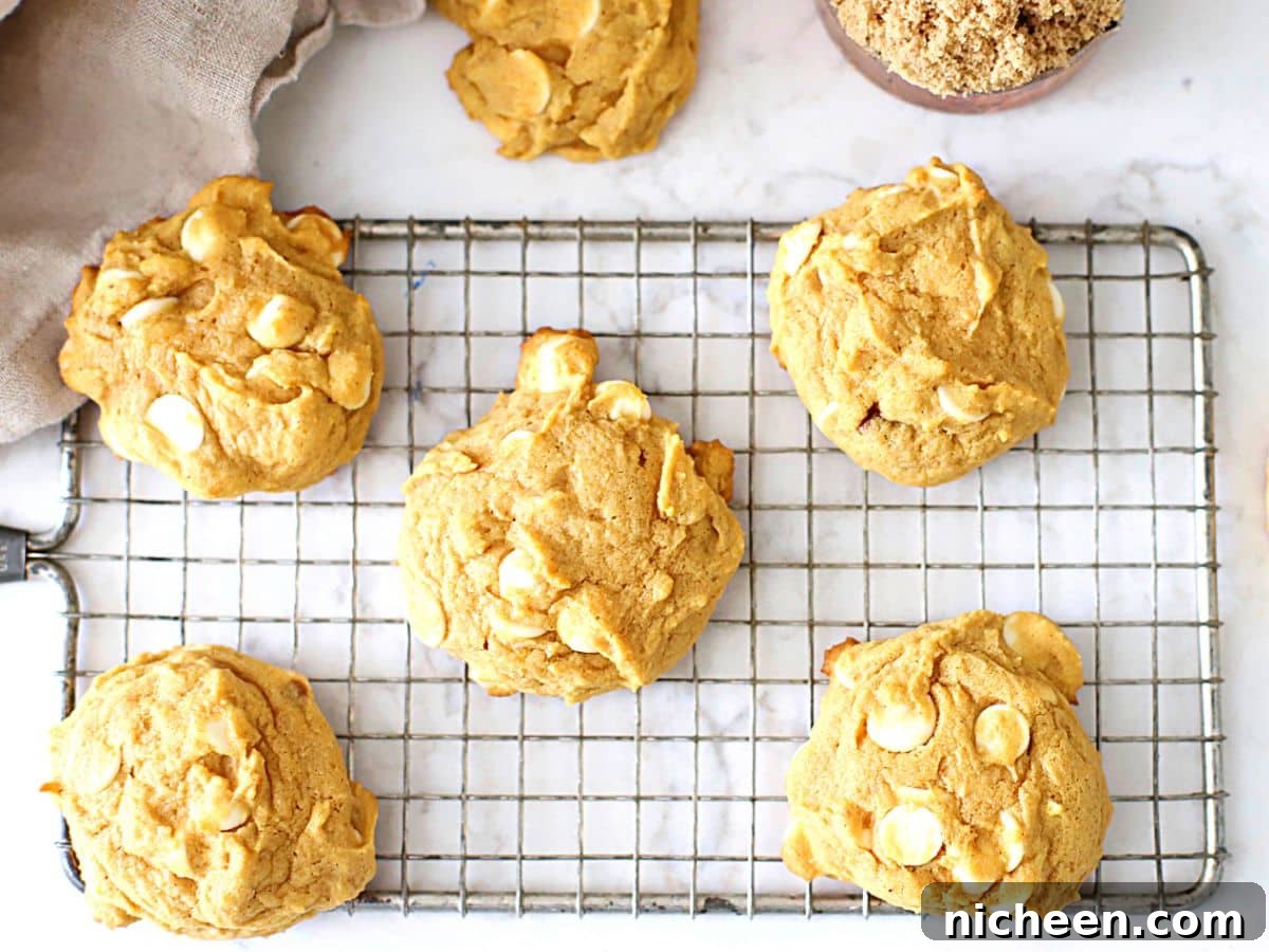 White Chocolate Chip Pumpkin Spice Cookies Recipe 3 Pumpkin cookies on a cooling rack.