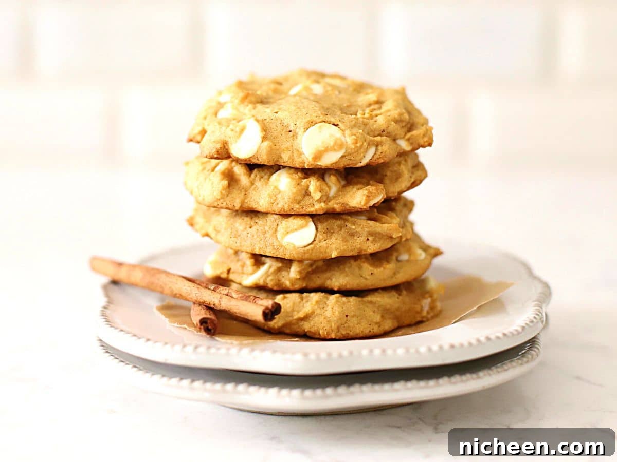 White Chocolate Chip Pumpkin Spice Cookies Recipe 4 Pumpkin cookies stacked on a plate.