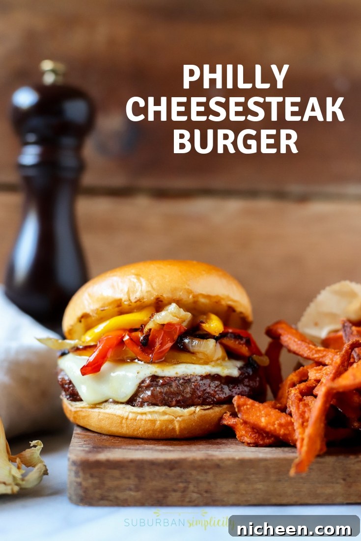 Homemade Philly Cheesesteak Burger Recipe 2 A burger topped with peppers, onions, and cheese next to sweet potato fries.