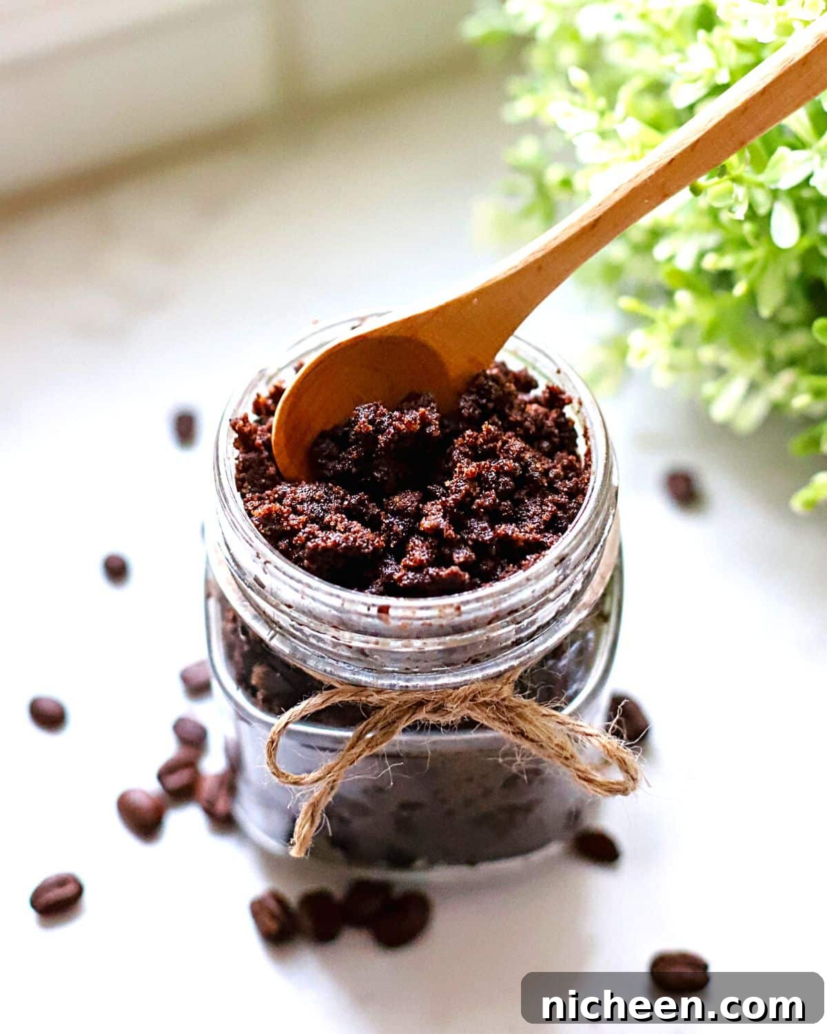 DIY Coffee Sugar Scrub Recipe for Glowing Skin 2 A coffee sugar scrub in a glass jar with a spoon sticking out of it.