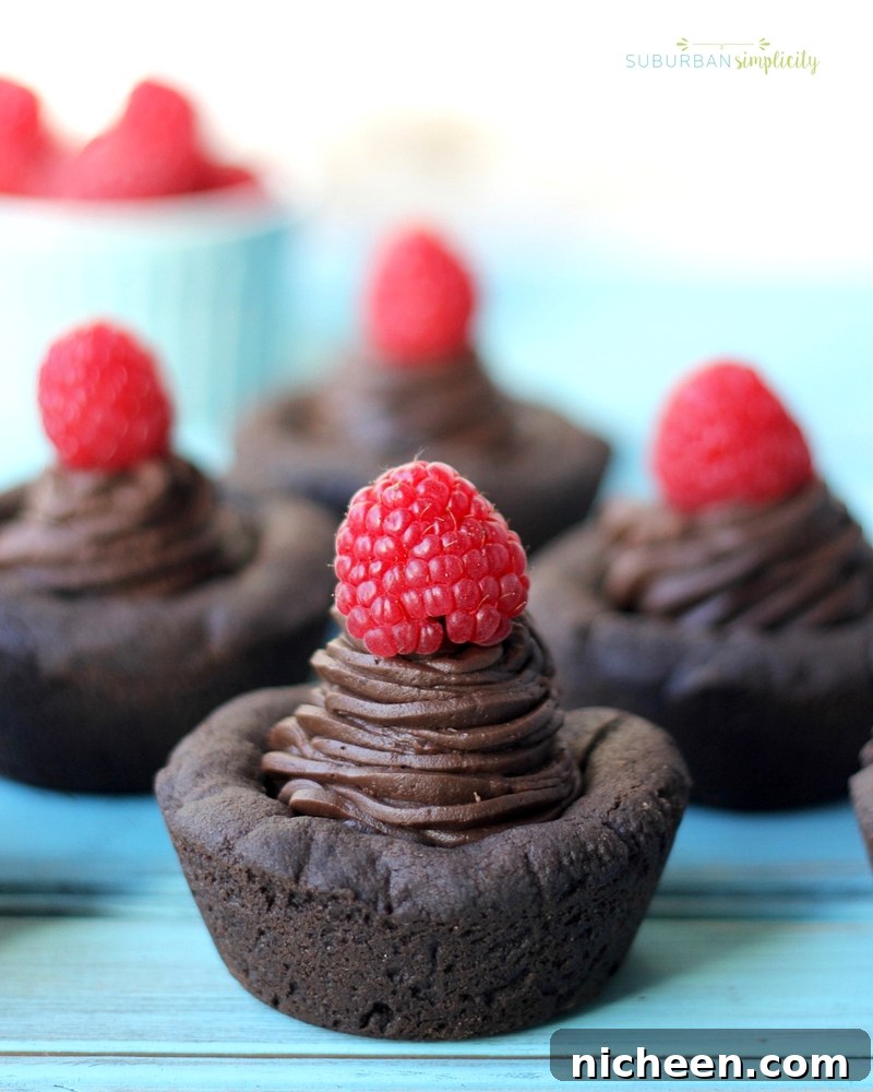 Four dark chocolate cookie cups topped with a red raspberry.