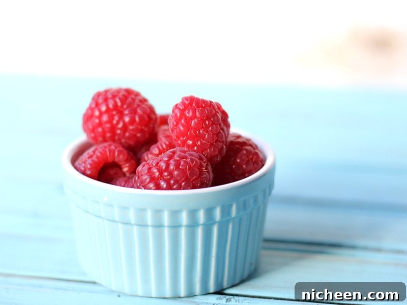 Ripe red raspberries in a small blue bowl.