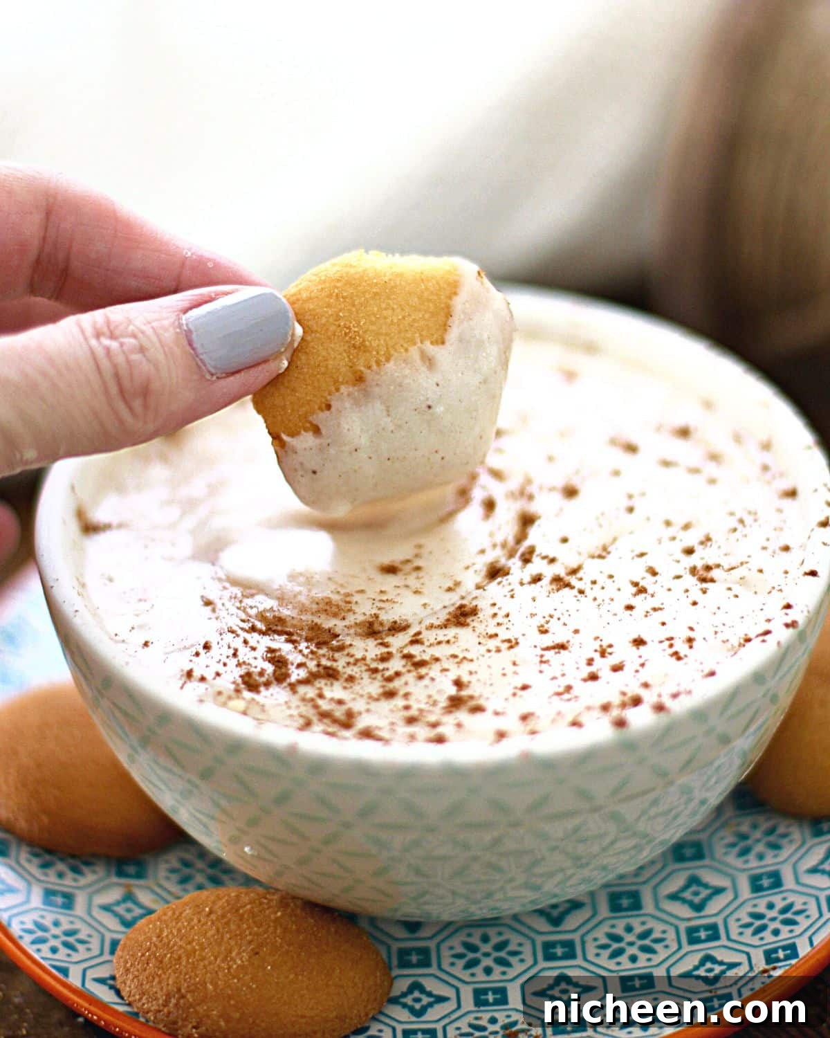A vanilla wafer dipping into eggnog dip.